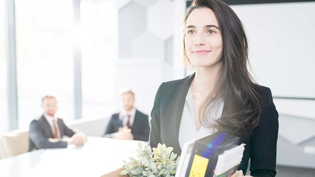 Attrition rates UK 2025. Picture shows smiling woman leaving her job with a box.